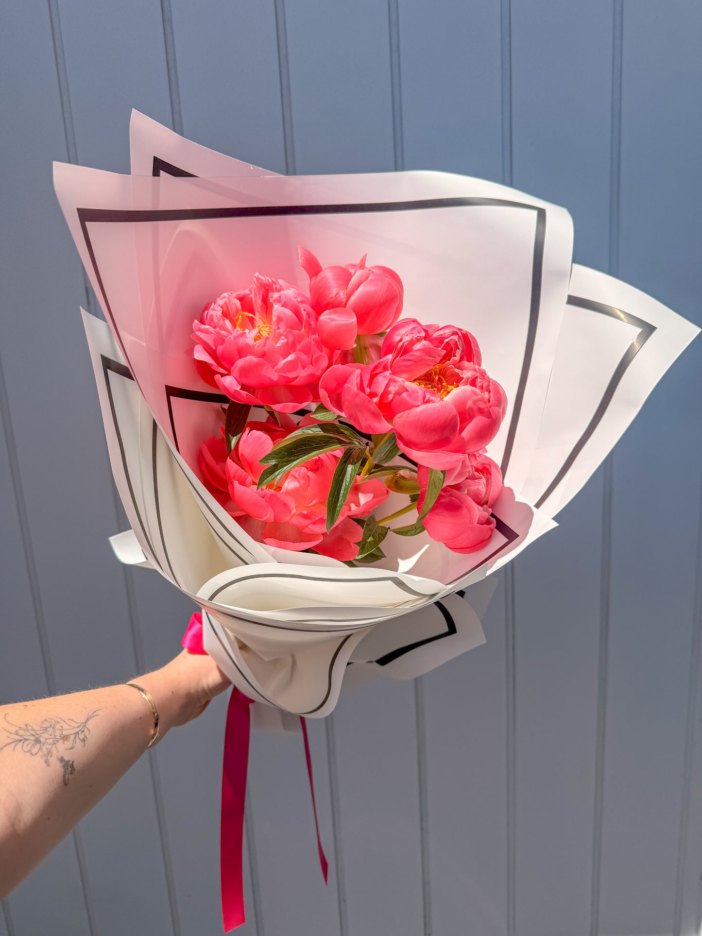 Coral pink peonies in black-edged white bouquet wrap with pink ribbon